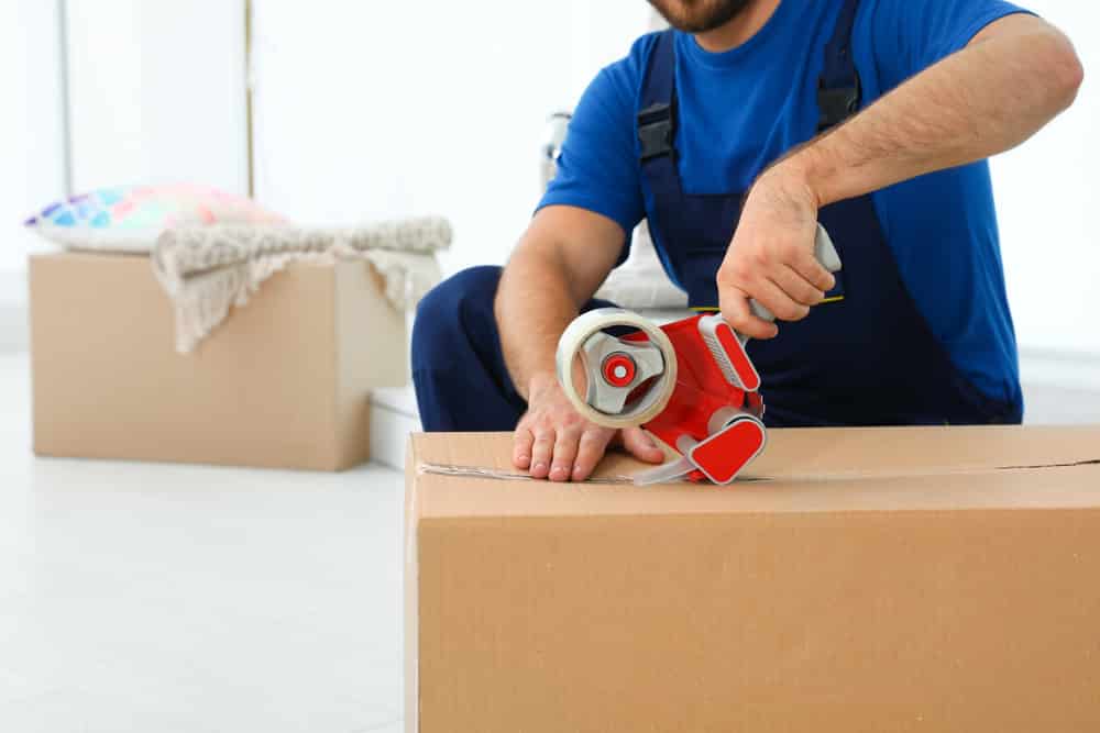 A Removalist Taping up a Cardboard Box for Moving